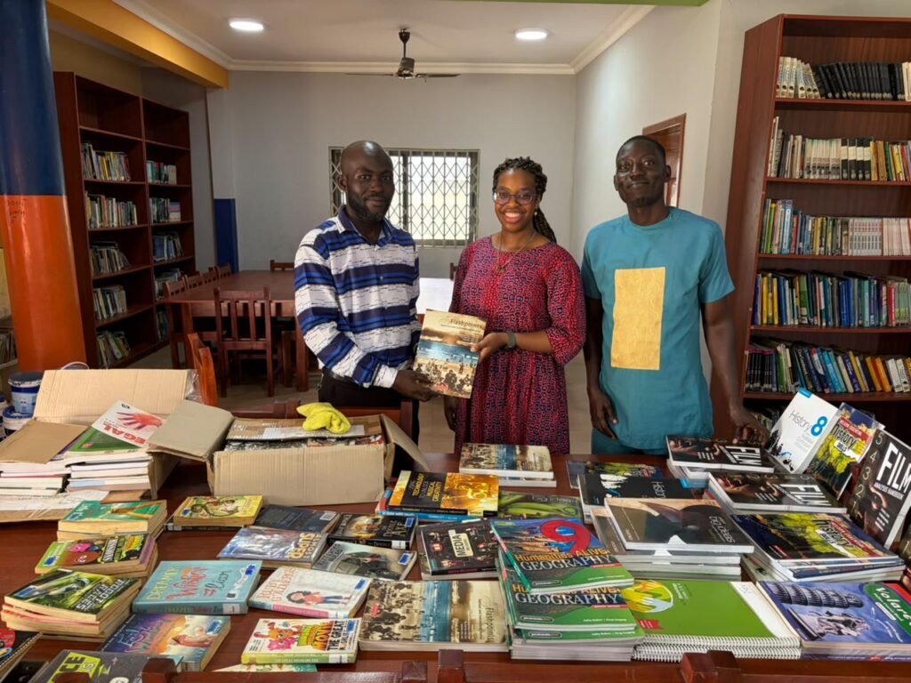 Three adults stand behind a table of donated books at the library presentation.